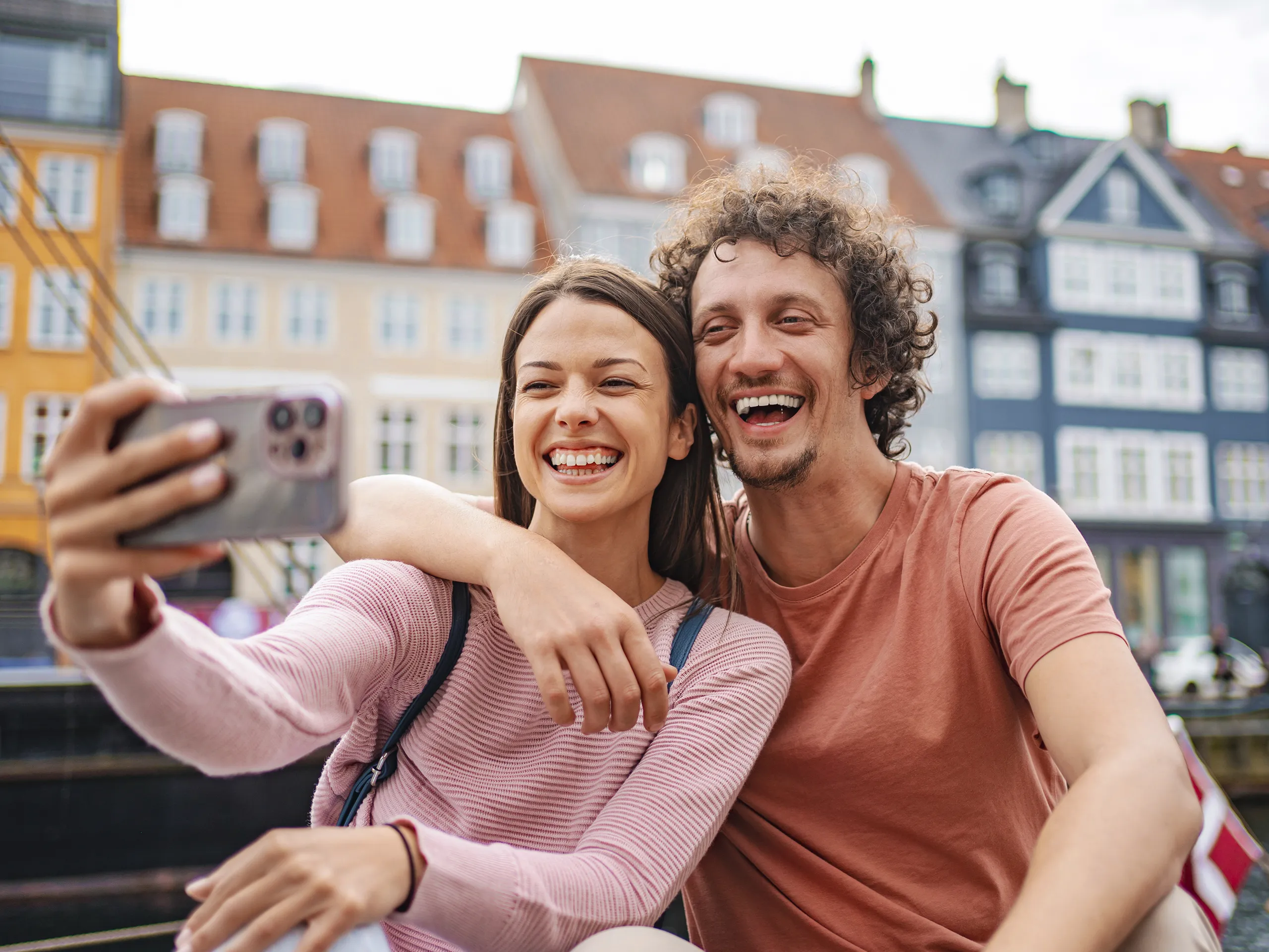 Smiling couple taking a selfie in front of historic buildings.