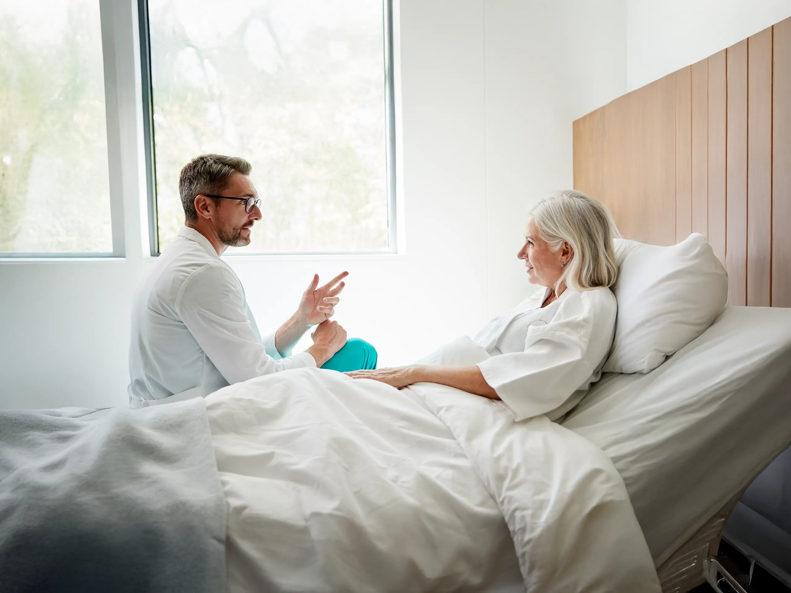 Un metge parla amb una pacient gran en un llit d'hospital.