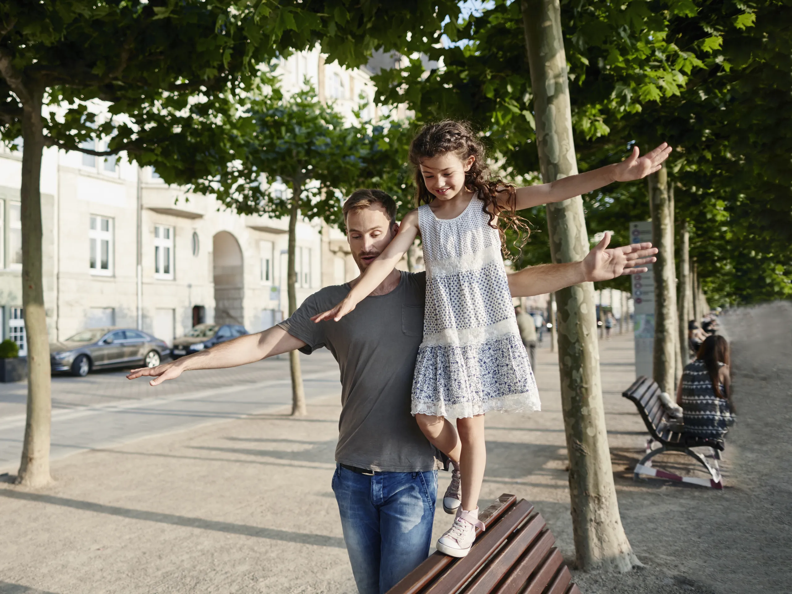 Un pare manté la seva filla en equilibri en un banc d'un parc a l'estiu.