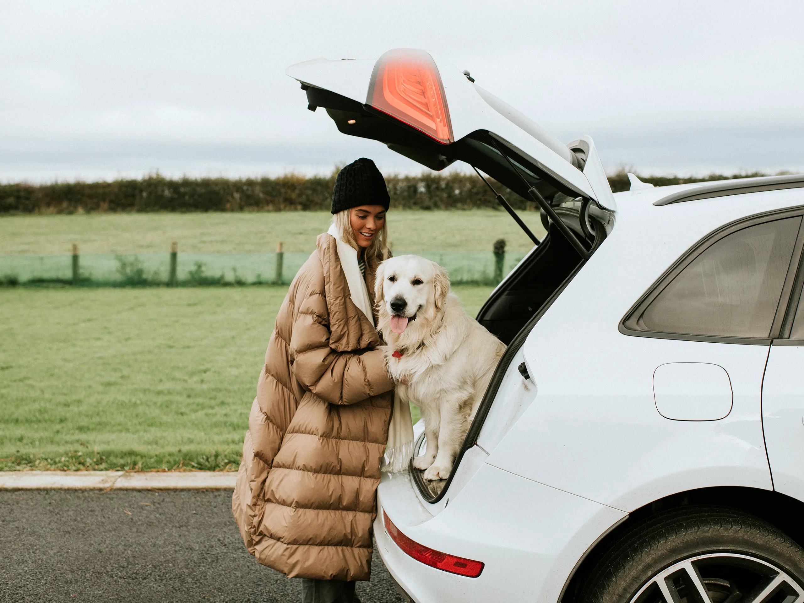 Una dona amb un golden retriever es troba al costat d'un cotxe amb el maleter obert.